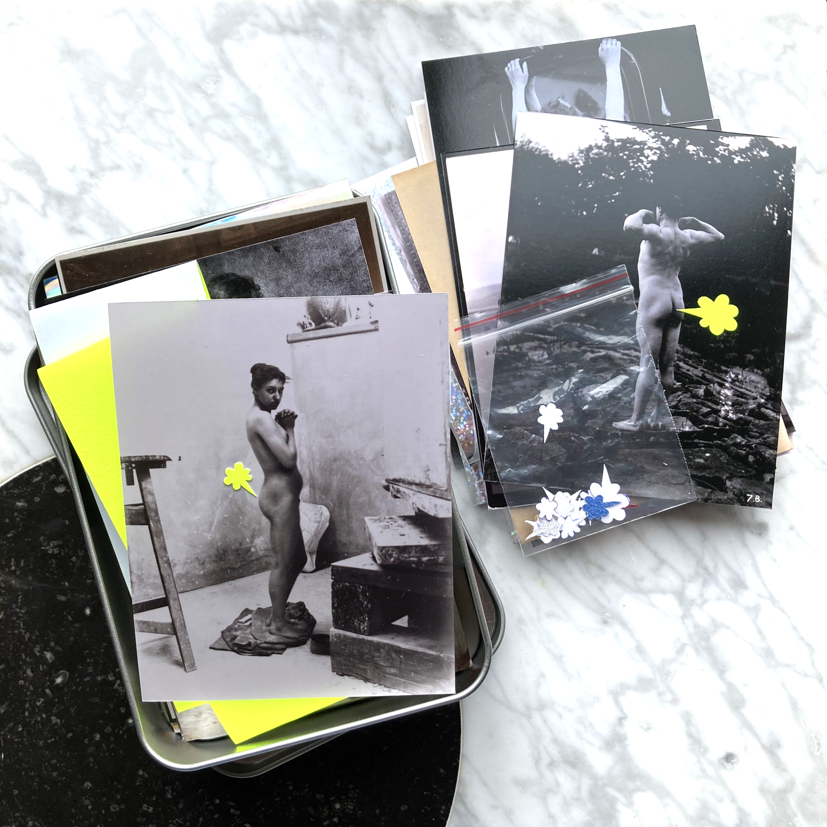 Two piles of black and white photographs of nude studies are displayed on a marble background. Playful yellow cartoon-style fart clouds are glued onto the photographs next to the person’s bum.