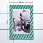 A 148x210mm poster featuring a photograph of a nude female standing in an art studio framed by a green and lilac striped border. A playful cartoon-style fart cloud, printed in holographic foil, is placed next to her bum.