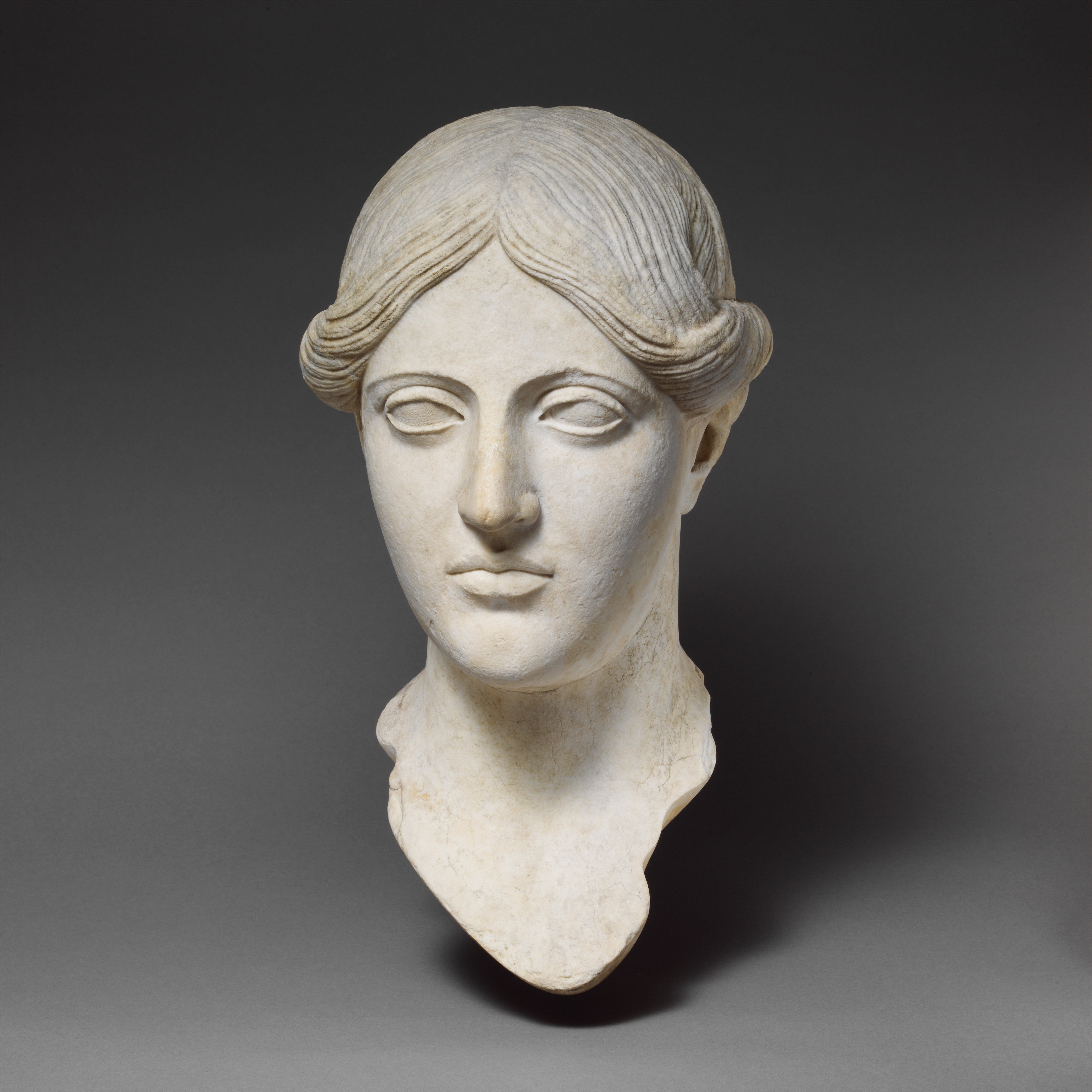 A marble statue head of a woman on a grey background.