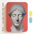 A unique art clock made of a printed statue head with yellow and blue eyes on a pink rectangular background. One eye is looking up, the other is looking down. Image text: ‘Psst... my eyes tell the time'.