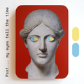 A unique art clock made of a printed statue head with yellow and blue eyes on a red rectangular background. One eye is looking up, the other is looking down. Image text: ‘Psst... my eyes tell the time'.