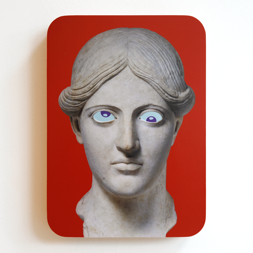 A printed statue head on a red rectangular background with blue eyes and purple pupils. One eye is looking up, the other eye is looking down.