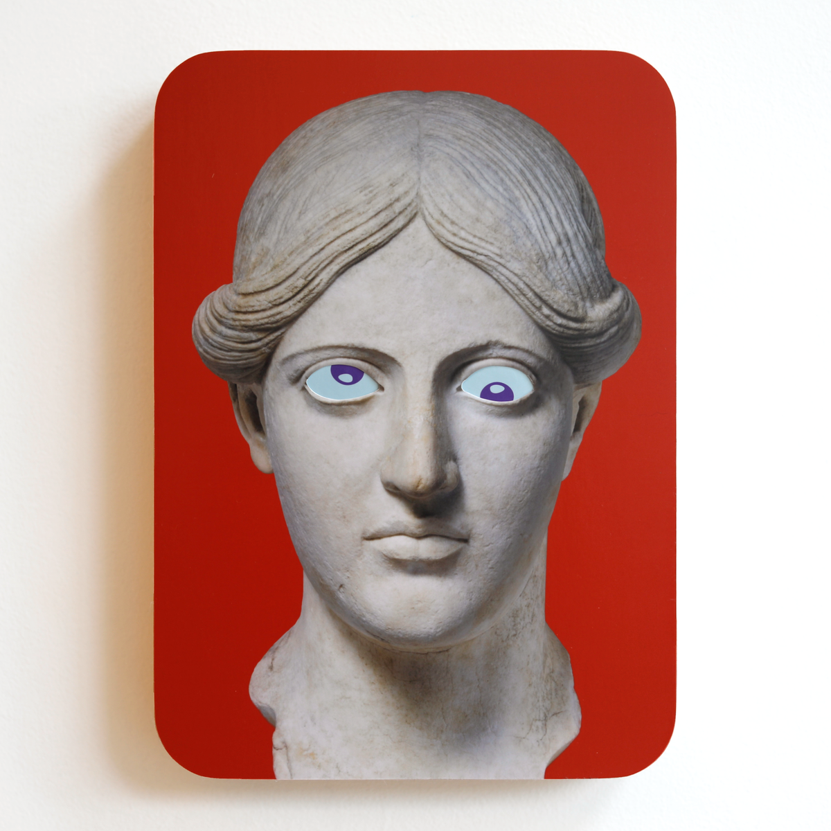 A printed statue head on a red rectangular background with blue eyes and purple pupils. One eye is looking up, the other eye is looking down.