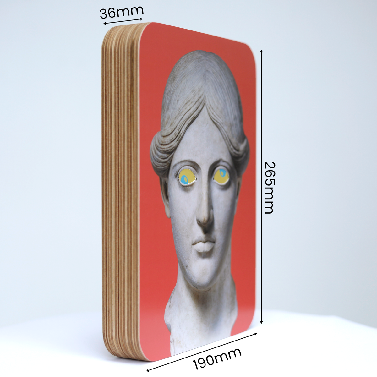 A Unique art clock made of a rectangular plywood body with a printed statue head on a pink background mounted onto the front face. The image shows the measurements which are: height 265mm, width 190mm and thickness 36mm.