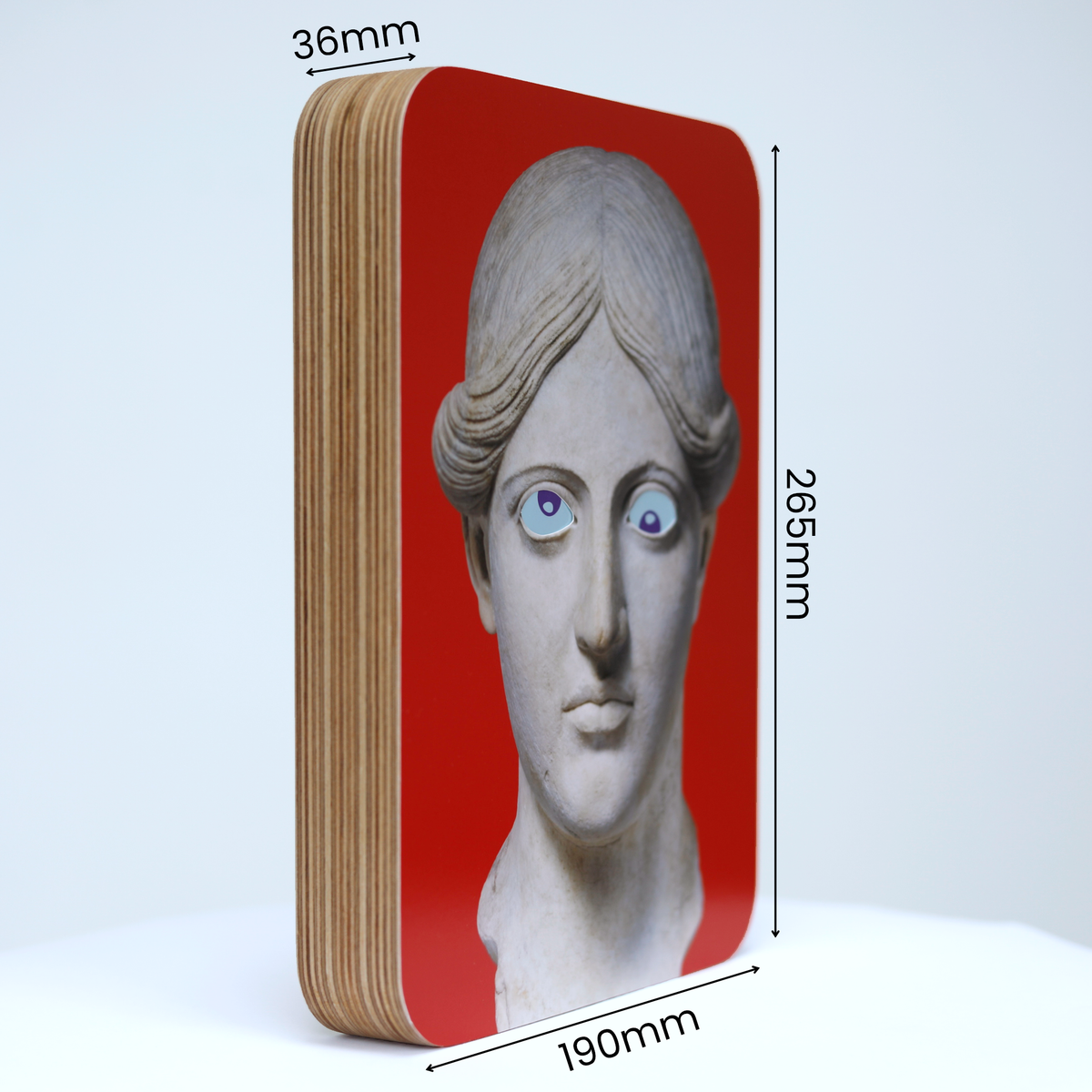 A unique art clock made of a rectangular plywood body with a printed statue head on a red background mounted onto the front face. The image shows the measurements which are: height 265mm, width 190mm and thickness 36mm.